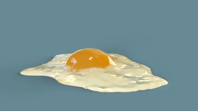 The yolk falls into a frying pan from a cracked raw egg, split by the