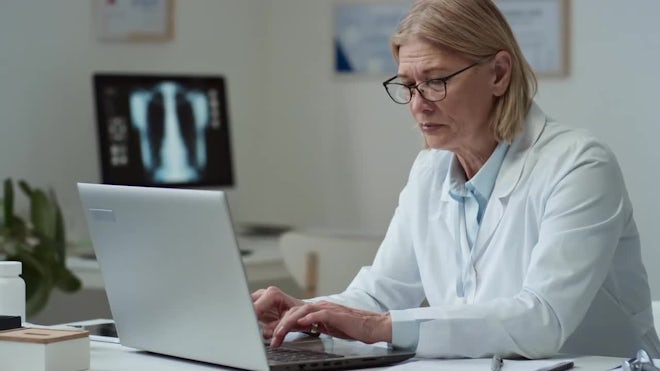 Mature Virtual Health Assistant Reading Medical Notes And Typing By Workplace - Stock Video | Motion Array