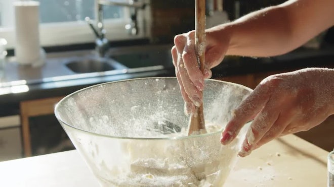 Baker using a wooden spoon to stir dough in mixing bowl stock