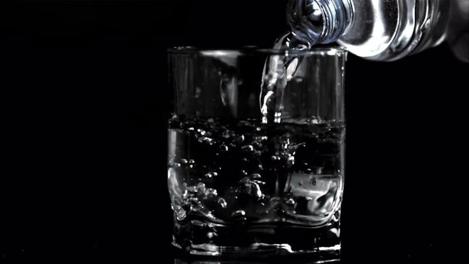 Short stem wine glass half full of water on a white background with a  reflection Stock Photo