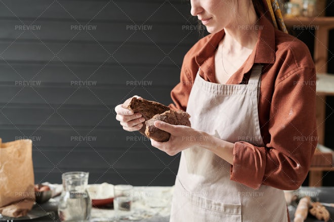 A baker woman holds fresh bread in her hand against the background of bakers  working in a bakery Stock Photo - Alamy