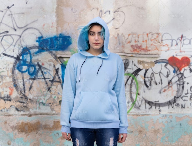 Blue haired Teenage girl in blue hoodie staying near graffiti wall with red water  bottle Stock Photo by katrinshine