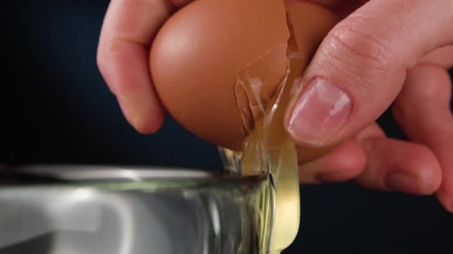 The yolk falls into a frying pan from a cracked raw egg, split by the