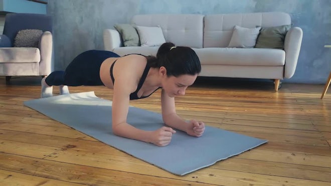 Slim woman in sportswear looking at camera while doing plank on mat in gym  stock photo