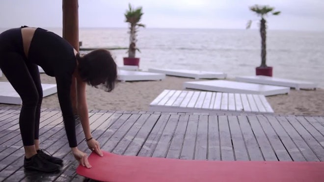 Woman Sets Yoga Mat, Beachside Calm. - Stock Video