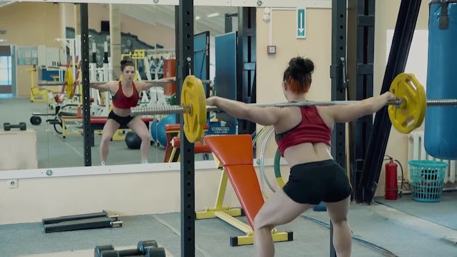 Young Petite Woman Performs The Exercise Squat With Barbell In The